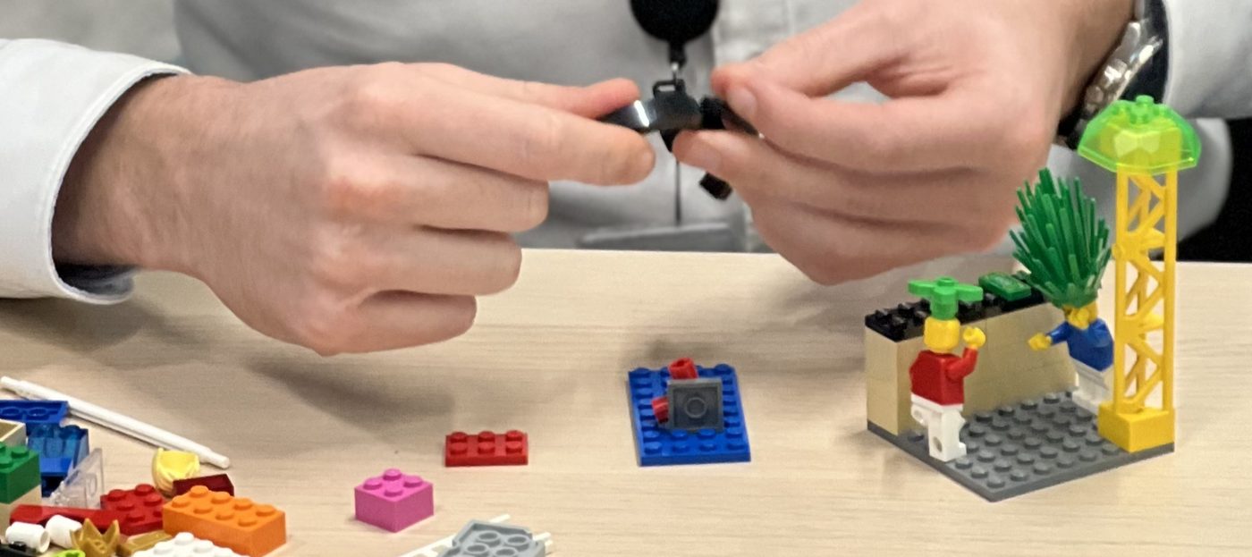 Deux mains assemblent des briques LEGO, à côté d'un petit modèle avec deux minifigurines